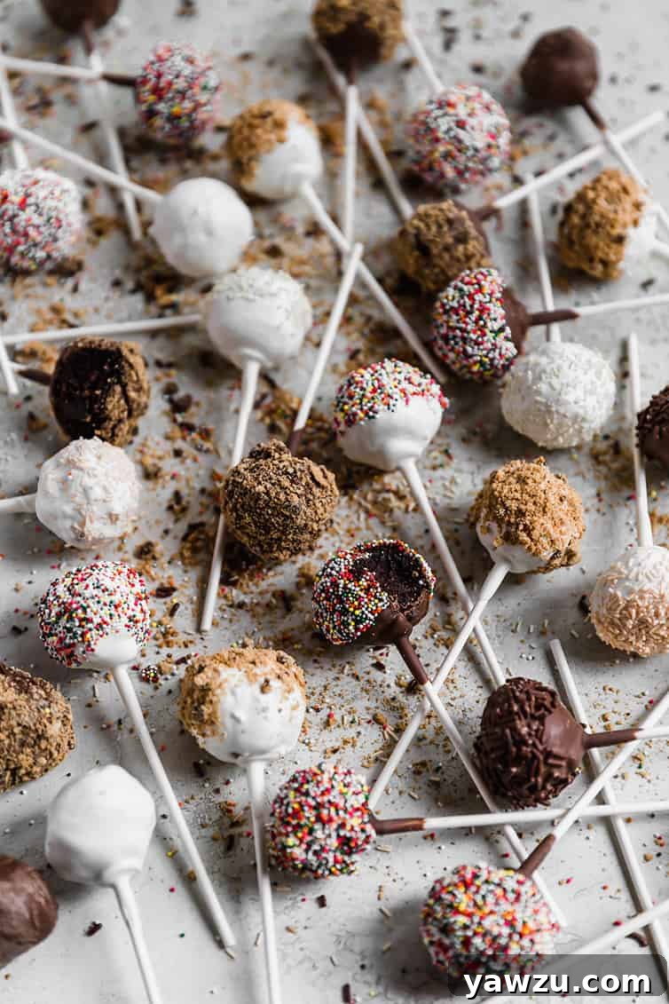 An overhead shot of numerous cake pops, dipped in white and milk chocolate and adorned with various toppings, artfully arranged on a surface.