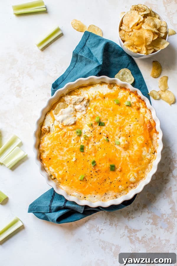 A baking dish filled with bubbling, cheesy buffalo chicken dip, surrounded by crunchy celery sticks and tortilla chips for dipping.