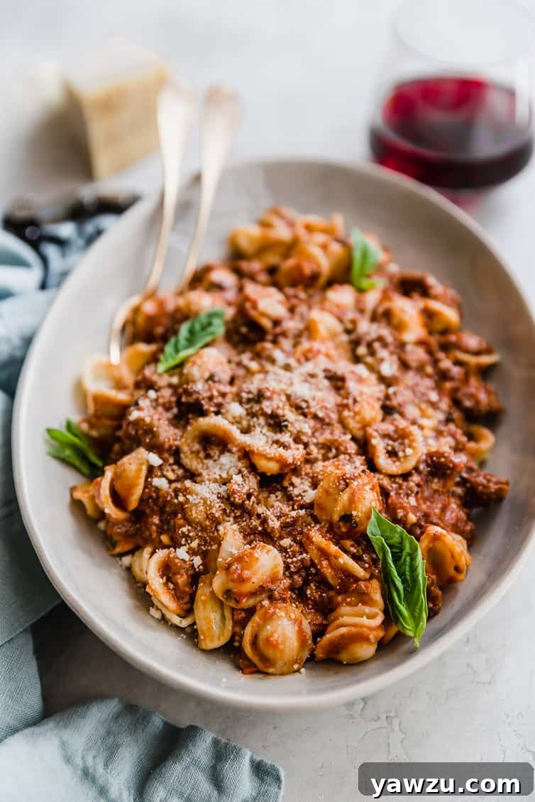 A bowl of pasta with rich bolognese sauce, garnished with fresh basil leaves.