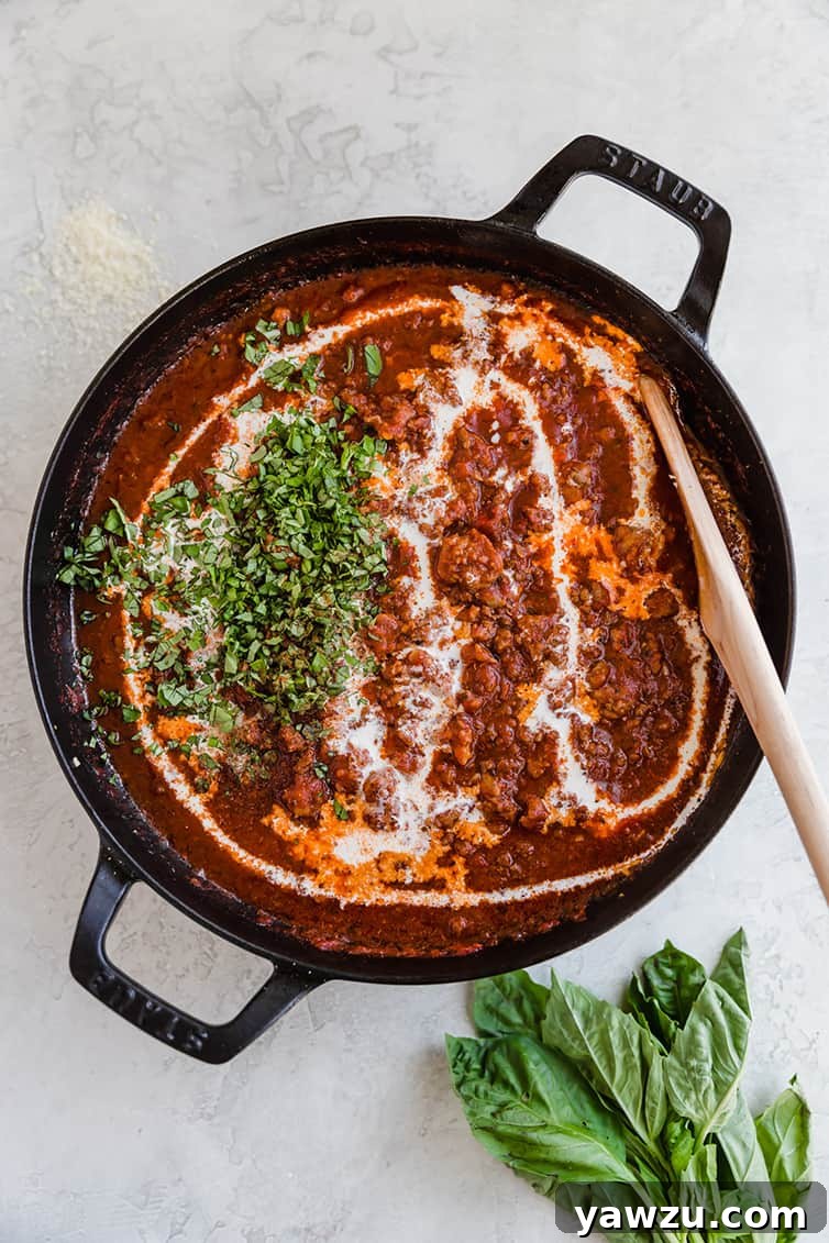 A pan of creamy bolognese sauce with fresh basil leaves stirred in.