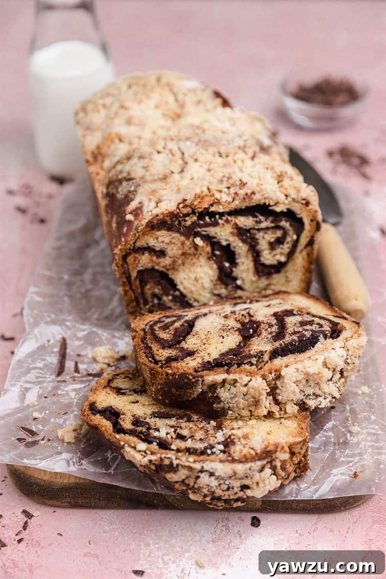 A beautifully baked loaf of chocolate babka with two slices expertly cut and displayed in front, showcasing its rich swirls.