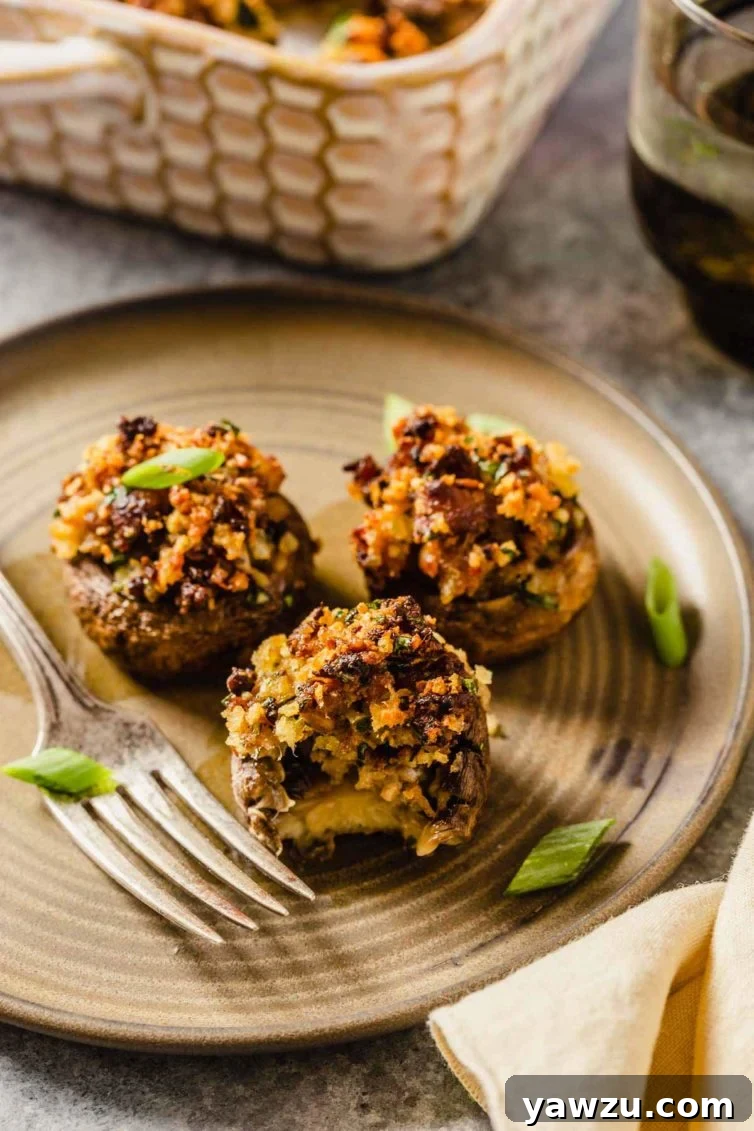 A small plate with three delicious sausage stuffed mushrooms, one with a bite taken out, resting next to a silver fork, inviting you to enjoy.