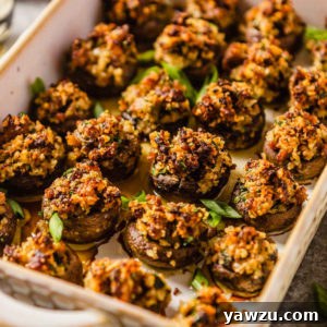 A rimmed baking dish with golden-brown sausage stuffed mushrooms garnished with fresh green onion, a perfect appetizer.