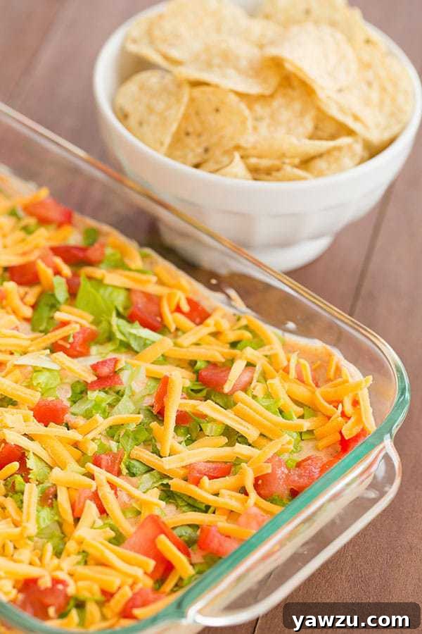 A festive seven-layer taco dip, generously topped with fresh ingredients and ready for a party.