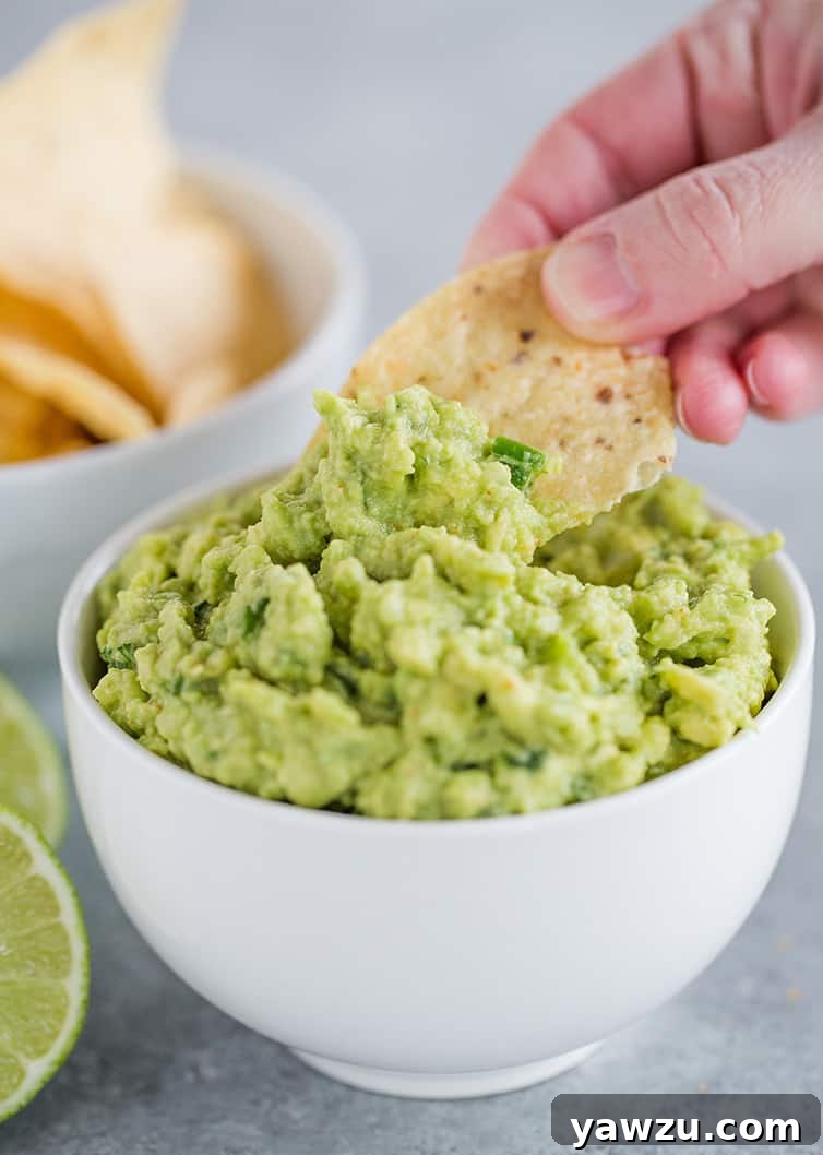 Someone dipping a tortilla chip into a vibrant bowl of freshly made guacamole, highlighting its creamy texture and rich green color.