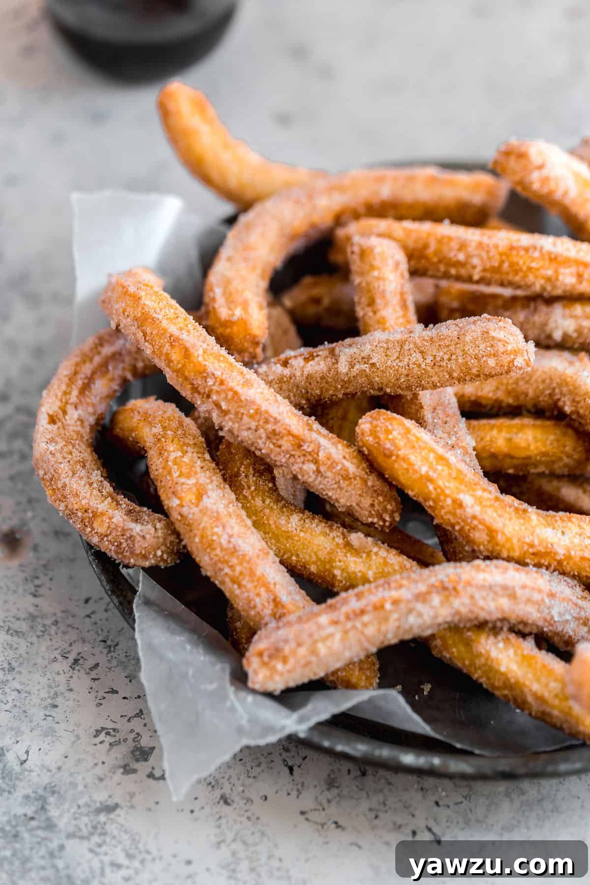 A black platter with parchment paper topped with fresh fried churros covered in cinnamon sugar.