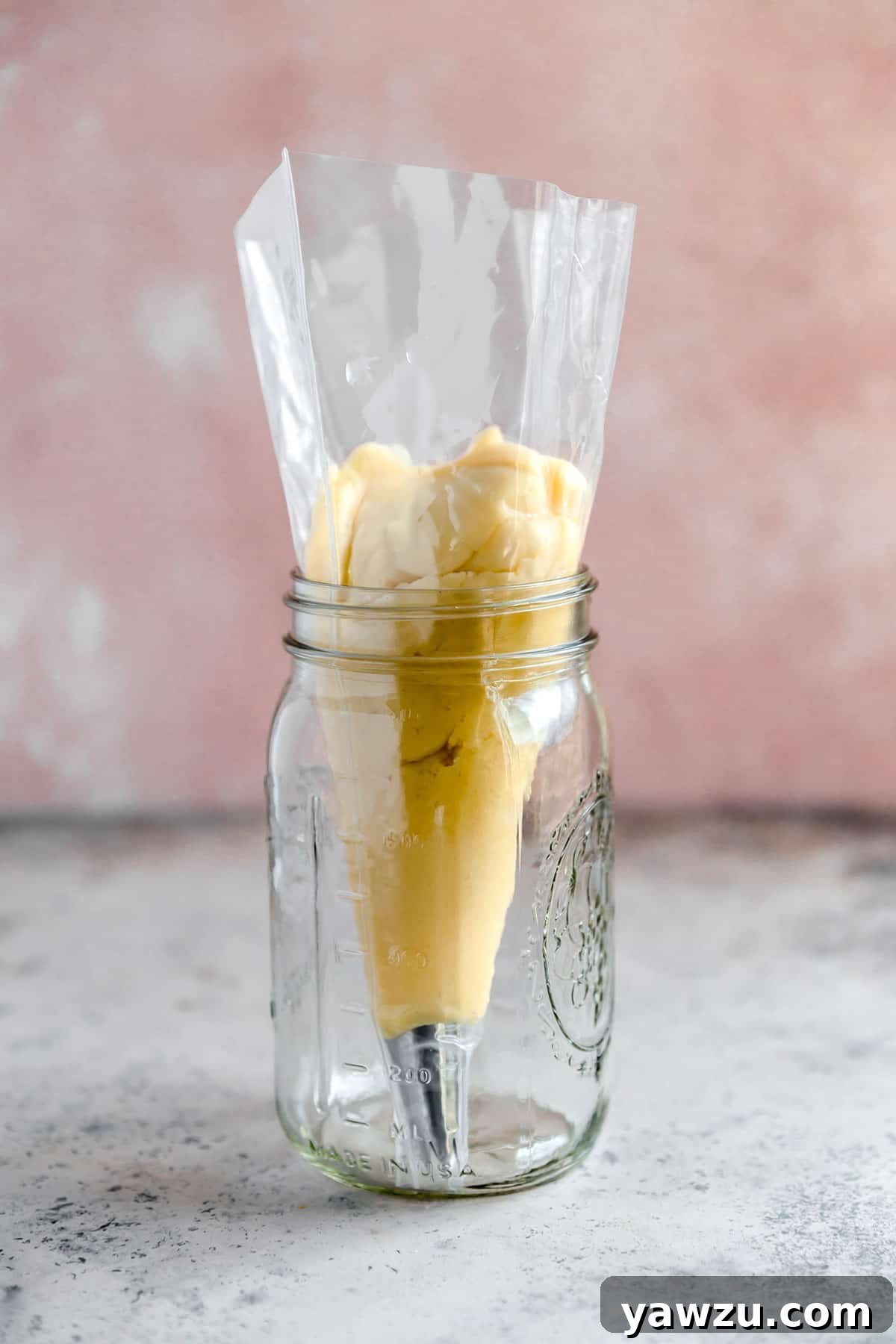 A pastry bag fitted with a star tip and filled with choux pastry in a mason jar to hold it up.