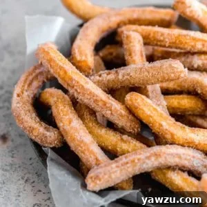 A pie pan lined with parchment paper and topped with fresh fried churros.