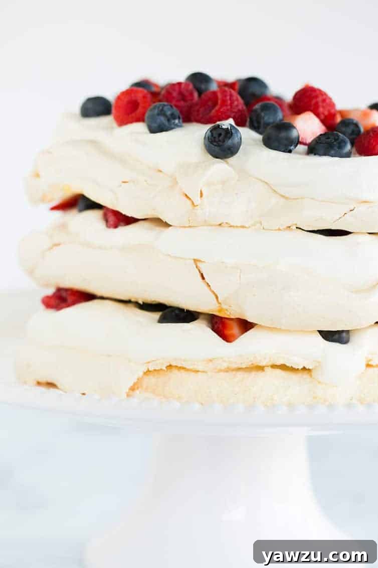 A close-up view of a delicate Pavlova Layer Cake, adorned with fresh whipped cream and an abundance of colorful berries.