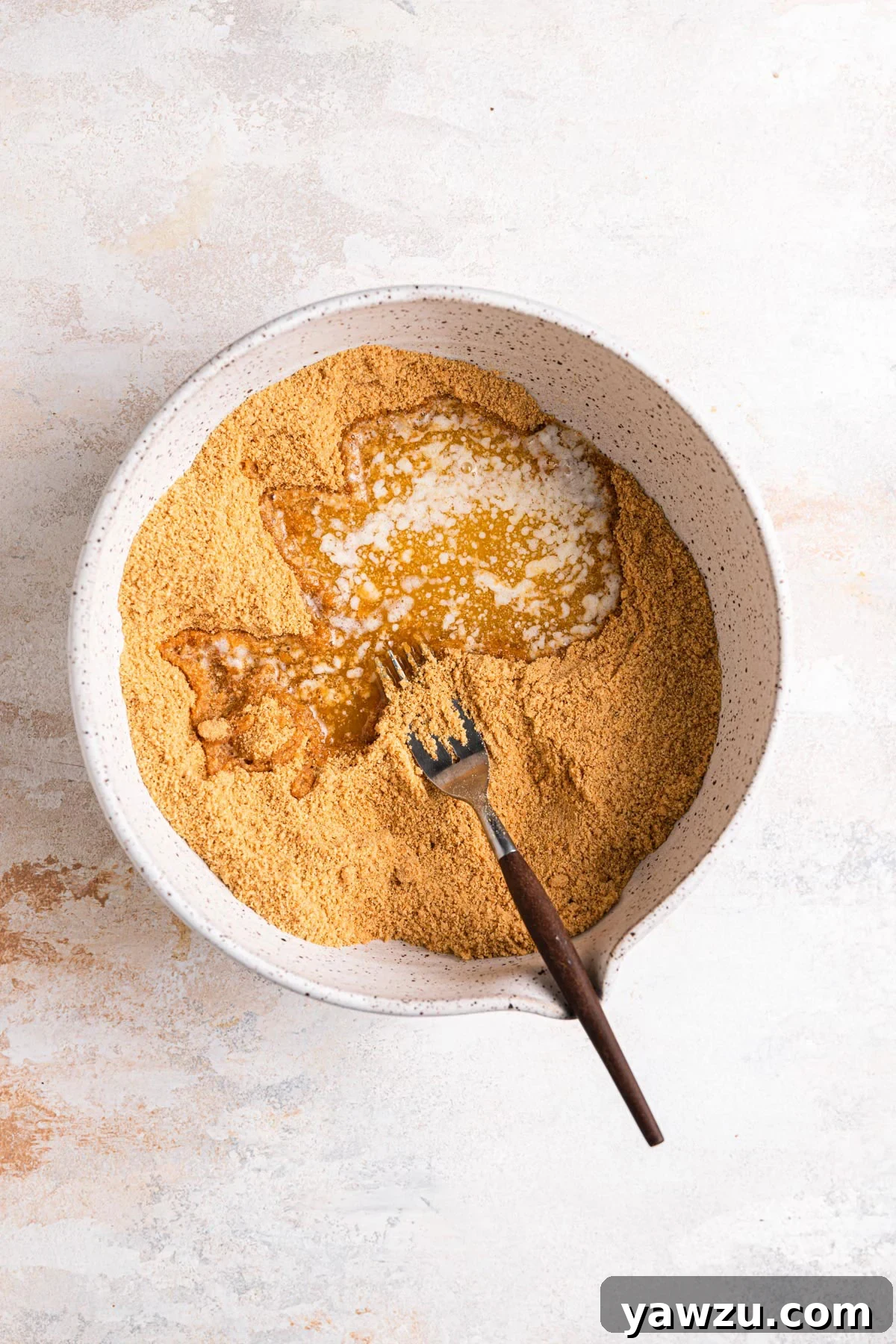 Melted butter added to bowl with graham cracker crumbs, brown sugar, and salt.