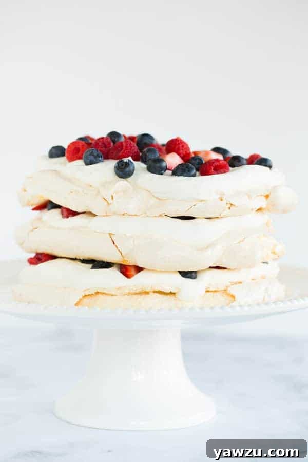 A stunning three-layered Pavlova cake, generously filled and topped with fresh whipped cream and an assortment of colorful berries, creating a light and airy summer dessert.