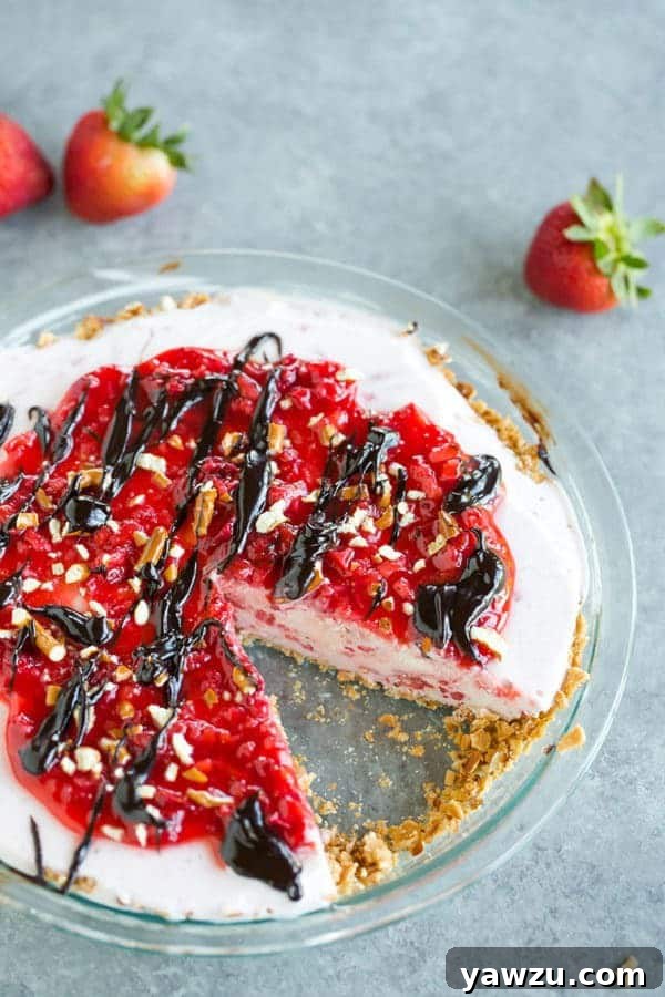 A refreshing strawberry-vanilla ice cream pie, featuring a unique sugar cone and pretzel crust, garnished with fresh strawberries and a drizzle of hot fudge sauce.