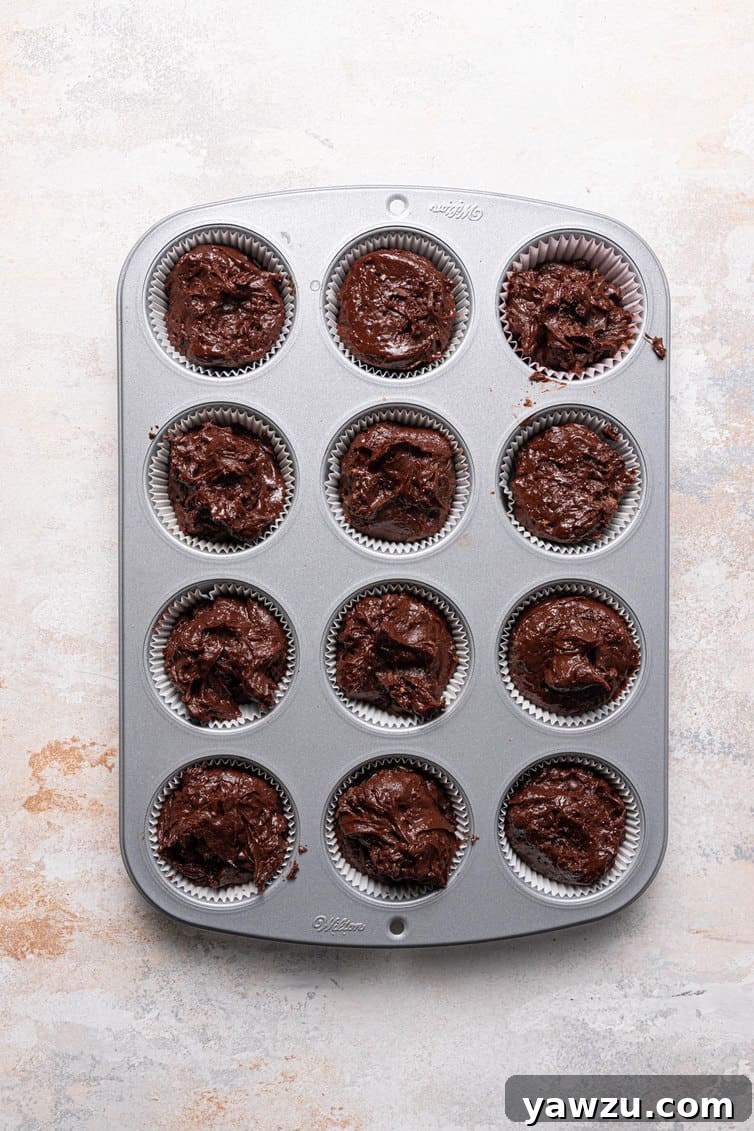 Close-up of thick, rich chocolate muffin batter perfectly portioned into a paper-lined muffin cup, ready for baking.