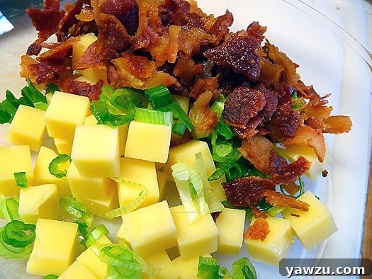 Assortment of fresh ingredients for Quiche Lorraine scones, including flour, eggs, cheese, and bacon, in a glass mixing bowl.