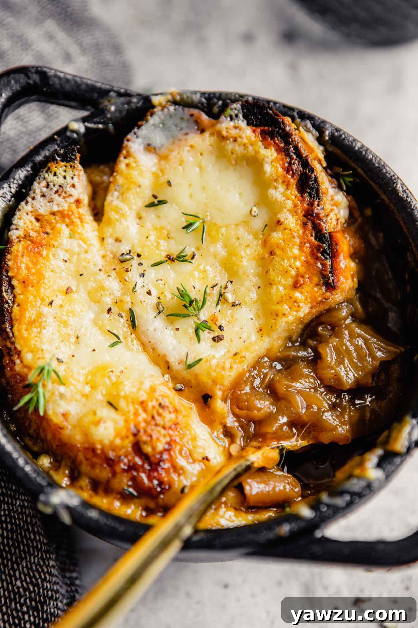A bowl of French onion soup with a spoon scooping out onions.