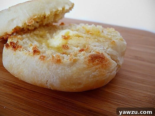 A stack of golden-brown homemade English muffins with melting butter