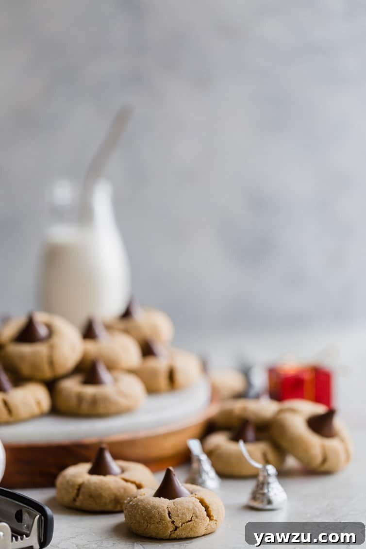 Classic Peanut Butter Blossoms arranged on a serving tray, accompanied by a glass of milk and scattered Hershey's kisses.