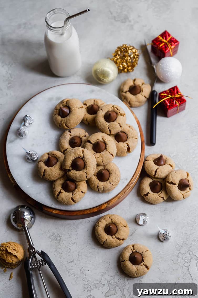 A beautifully presented serving of Peanut Butter Blossoms on a round tray, with a glass of milk and more Hershey's Kisses nearby.