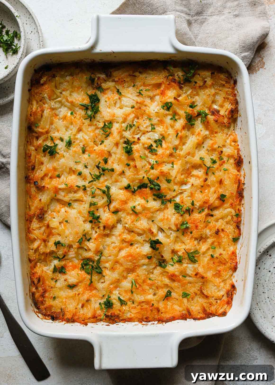 Overhead photo of a golden-brown, cheesy hashbrown casserole garnished with fresh parsley in a white baking dish.