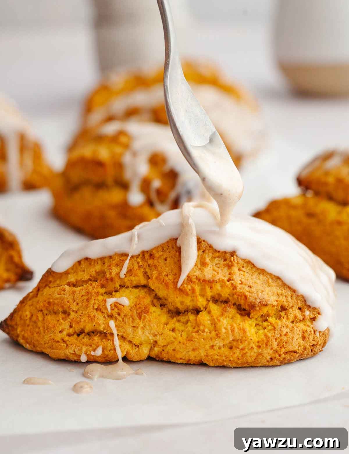 A spoon drizzling spiced glaze onto a pumpkin scone.