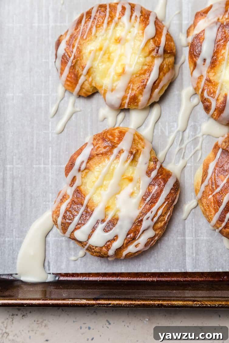 Freshly baked cream cheese Danish pastries arranged on a baking sheet, elegantly drizzled with a sweet white glaze.