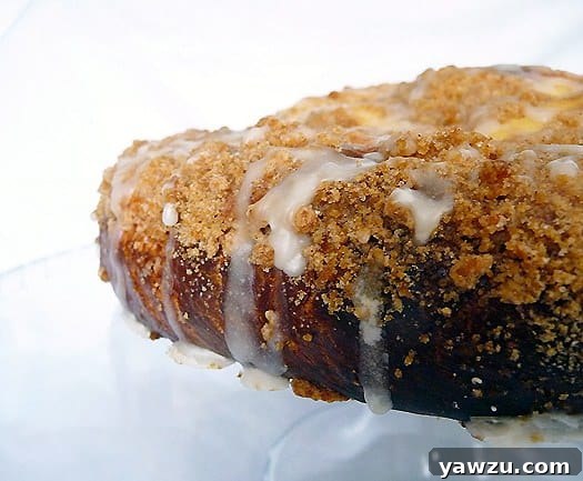 Side view of coffee cake with sweet cheese filling and vanilla icing on a glass cake stand.