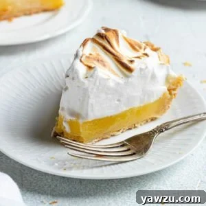 A slice of lemon meringue pie on a white plate with a fork.