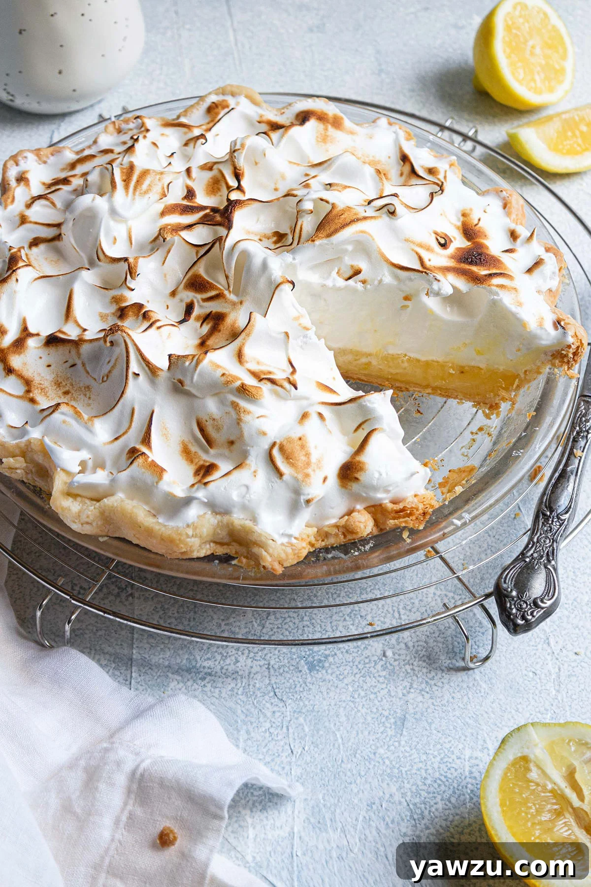 A beautifully baked lemon meringue pie in a classic glass pie plate, with one perfect slice already removed, revealing the distinct layers of crust, filling, and meringue.