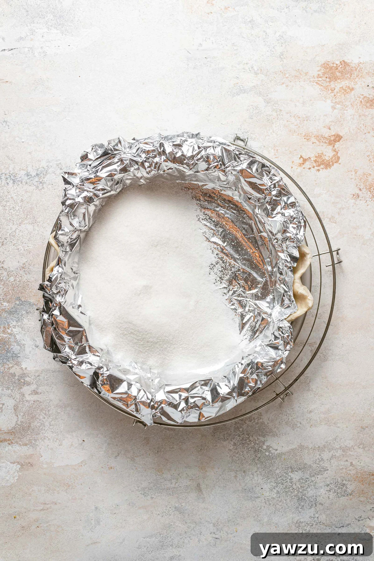 A pie crust being blind baked in an oven, fully covered with aluminum foil and weighted down, ensuring an even bake.
