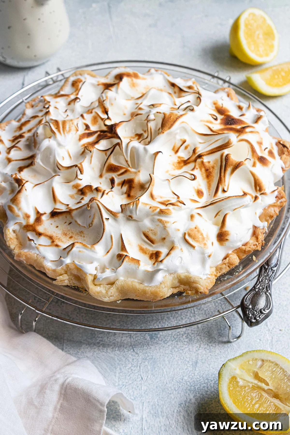 A fully baked lemon meringue pie with a golden-brown, beautifully peaked meringue topping, signifying its readiness for cooling and chilling.