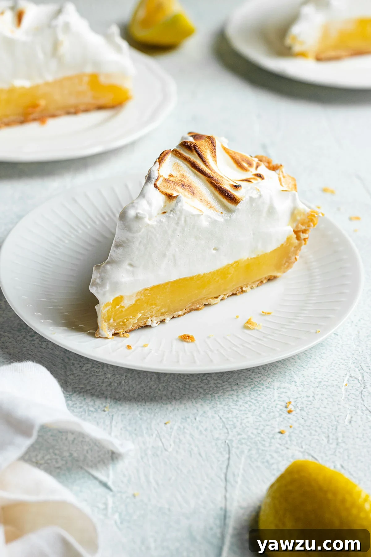 A beautifully presented slice of lemon meringue pie on a white plate, showcasing its golden crust, bright lemon filling, and airy, toasted meringue topping.
