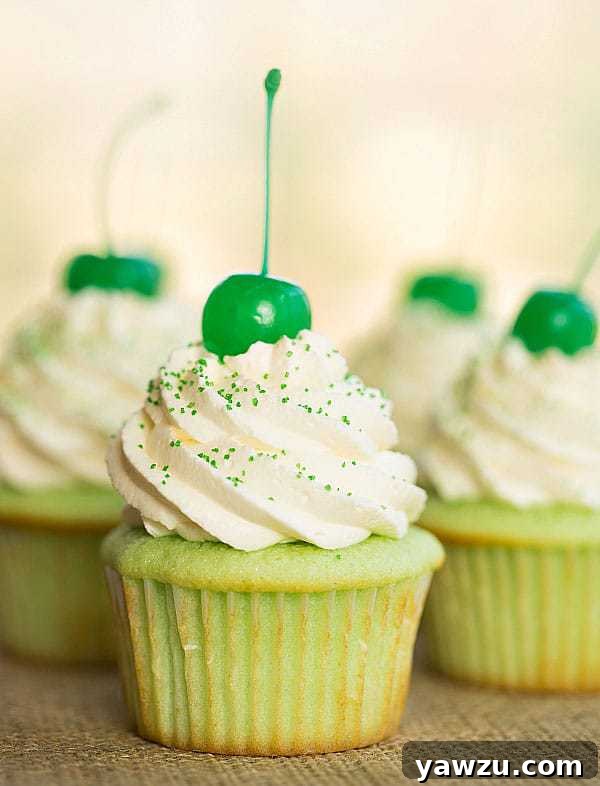 A plate of adorable Shamrock Shake Cupcakes, featuring vibrant green vanilla-mint cake topped with fluffy whipped cream frosting and sprinkles, perfect for a St. Patrick's Day party.
