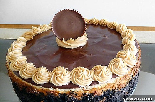 A stunning whole Peanut Butter Fudge Cheesecake, elegantly presented on a cake stand and ready to be sliced, garnished with a Reese's Big Cup.