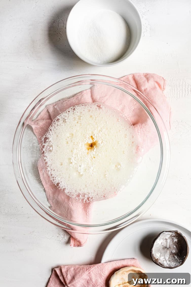 Close-up of vanilla extract being added to frothy egg whites in a mixing bowl.
