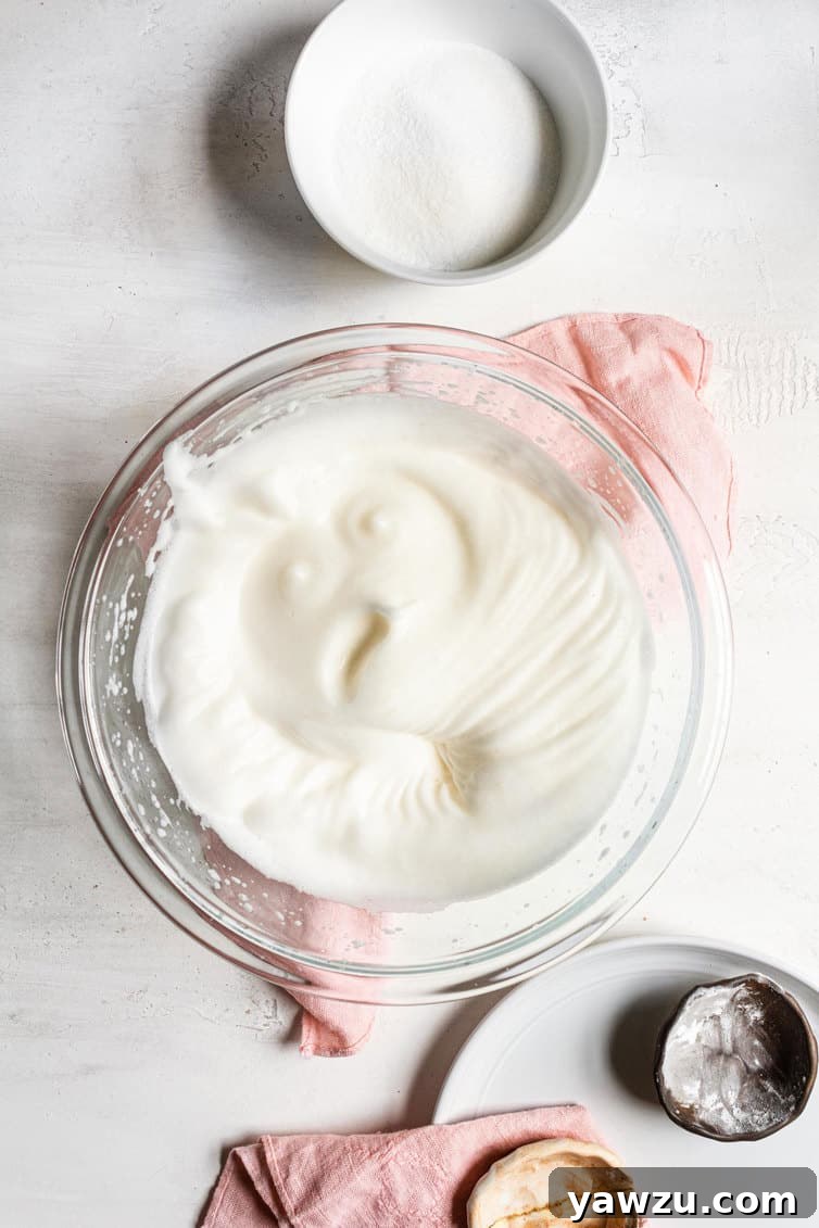 Egg whites whipped to soft peaks in a clear glass mixing bowl, light and fluffy.