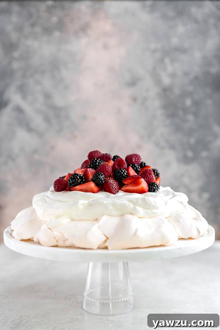 A beautiful pavlova adorned with whipped cream and fresh berries, ready to serve on a glass cake plate.