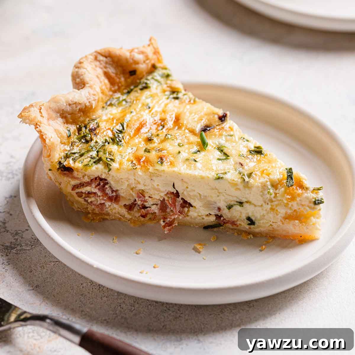 Side view of a slice of quiche on a white plate.