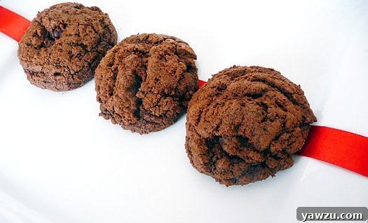 Three decadent triple chocolate cookies arranged on a pristine white plate, inviting indulgence.