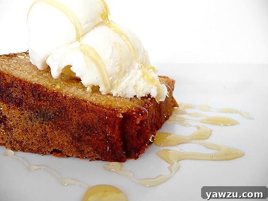 Side view of a luscious slice of Honey-Vanilla Sour Cream Pound Cake, elegantly topped with a scoop of creamy vanilla ice cream and a glistening drizzle of golden honey, presented on a pristine white plate.