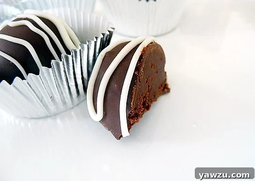 A rich dark chocolate truffle, perfectly cut in half to reveal its smooth, creamy ganache interior, resting on a white plate.