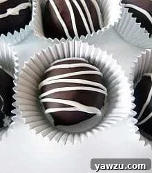 Six decadent dark chocolate truffles arranged elegantly in paper candy liners on a crisp white plate.