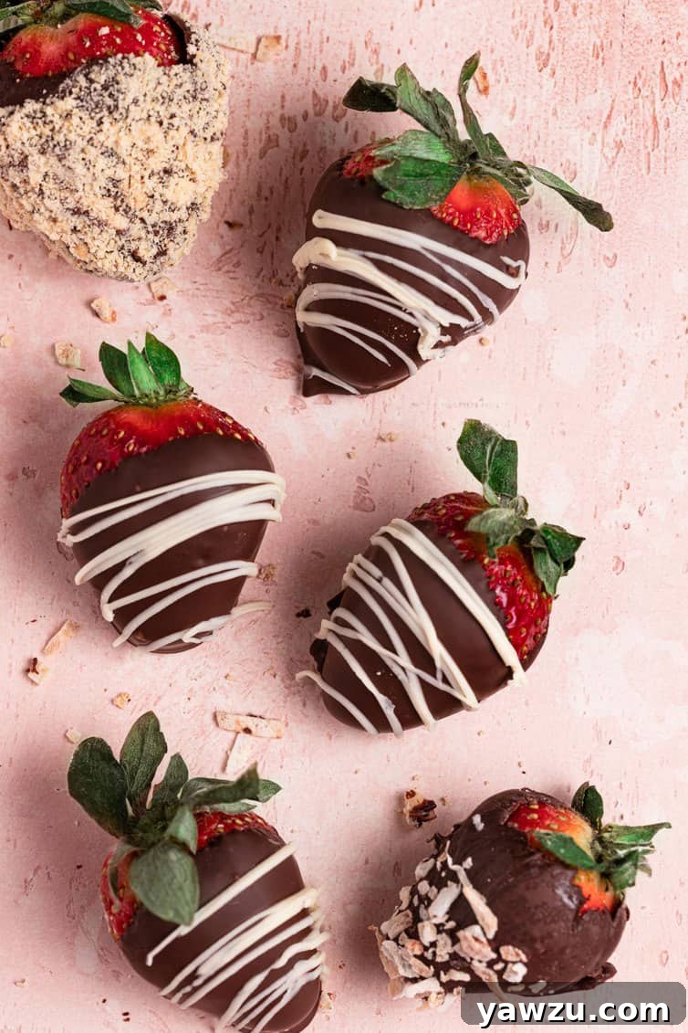 Six chocolate covered strawberries topped with chocolate drizzles and crushed nuts on a pink counter, showcasing their gourmet appeal and inviting texture.