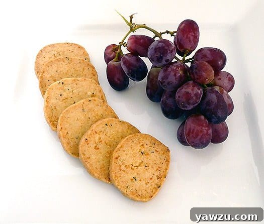 Golden Parmesan and thyme crackers resting on a white plate, accompanied by a bunch of fresh grapes, ready to be served.