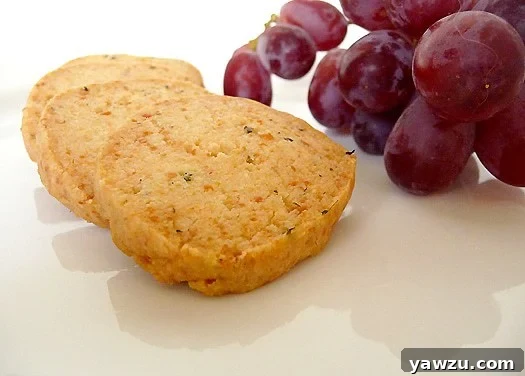 An inviting close-up of perfectly baked Parmesan and thyme crackers arranged on a white plate, garnished with fresh grapes, ready to be enjoyed.