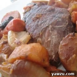 Pot roast with cooked potatoes, carrots, onions, and mushrooms on a plate.