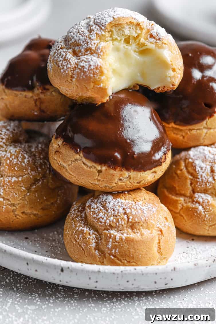 A white speckled plate piled high with cream puffs with one on the top with a bite out.