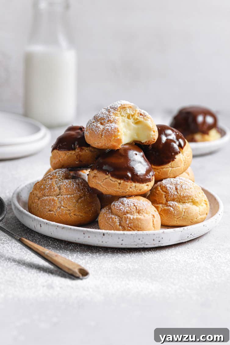 A white plate with cream puffs in a pile and a spoon to the left with a jug of milk in the back.