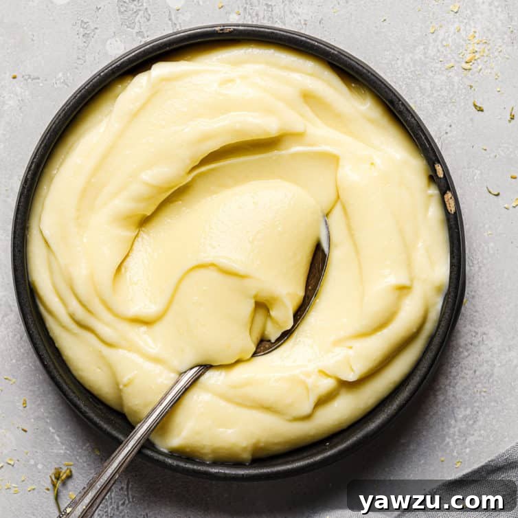 Top down photo of a black bowl with pastry cream and a silver spoon scooping pastry cream in the bowl.