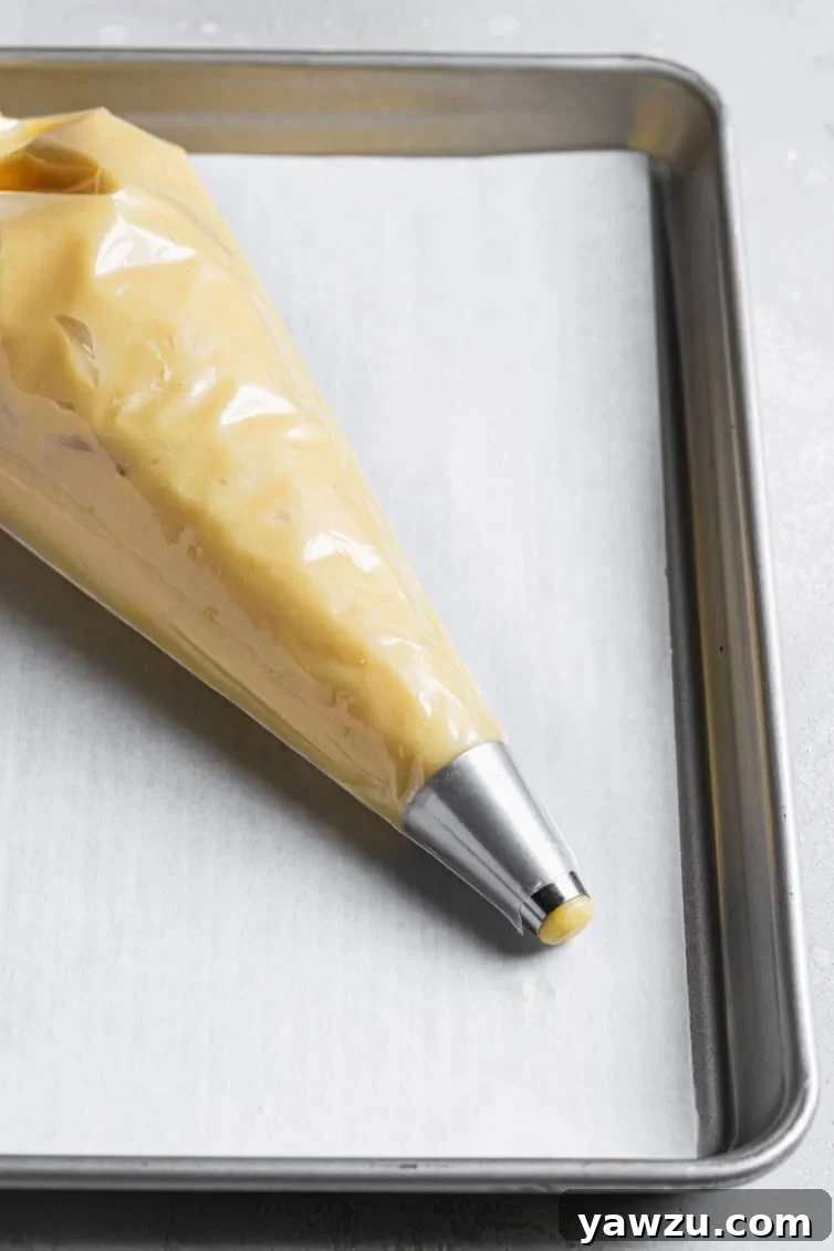 Pastry bag fitted with a round pastry tip and filled with choux pastry dough.