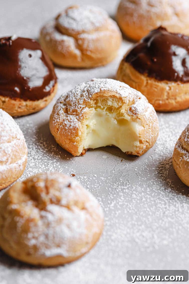 Cream puffs with powdered sugar and chocolate glaze on a counter with one in the middle missing a bite.